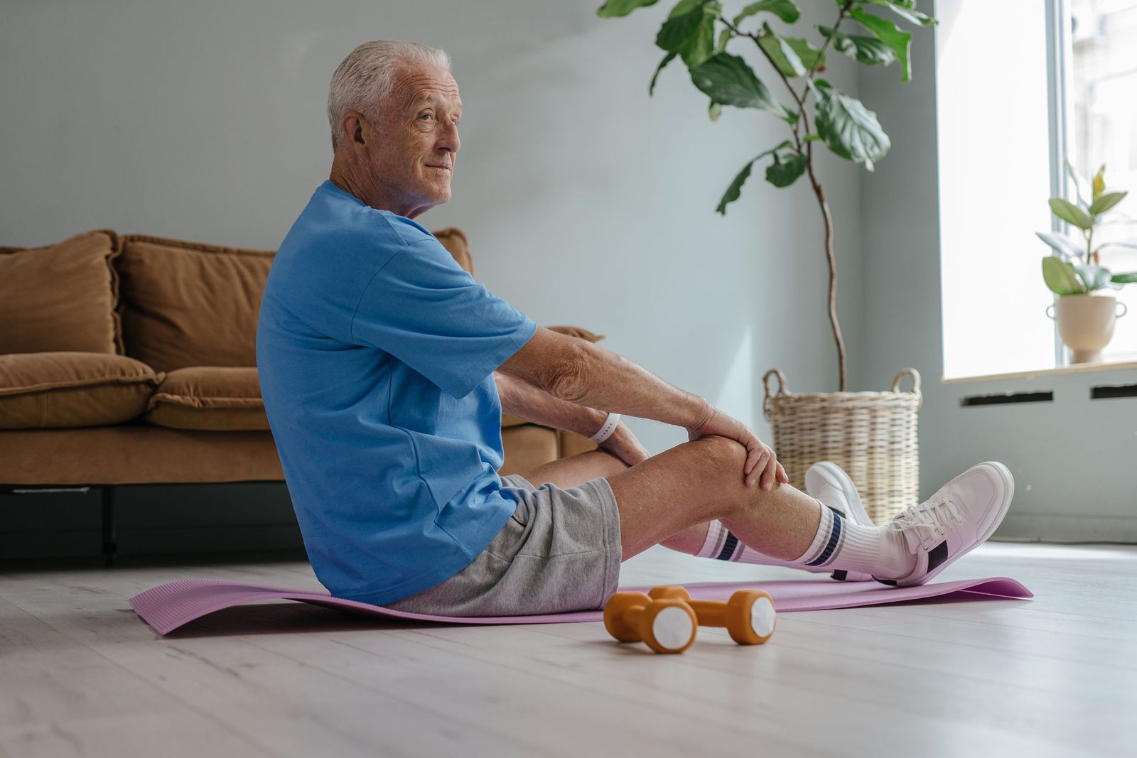 Äldre man sitter på en träningsmatta i vardagsrummet och håller om knät